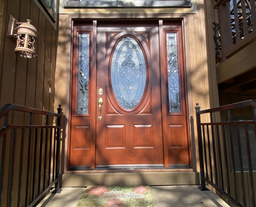 A brown front door with oval glass and a window on each side.